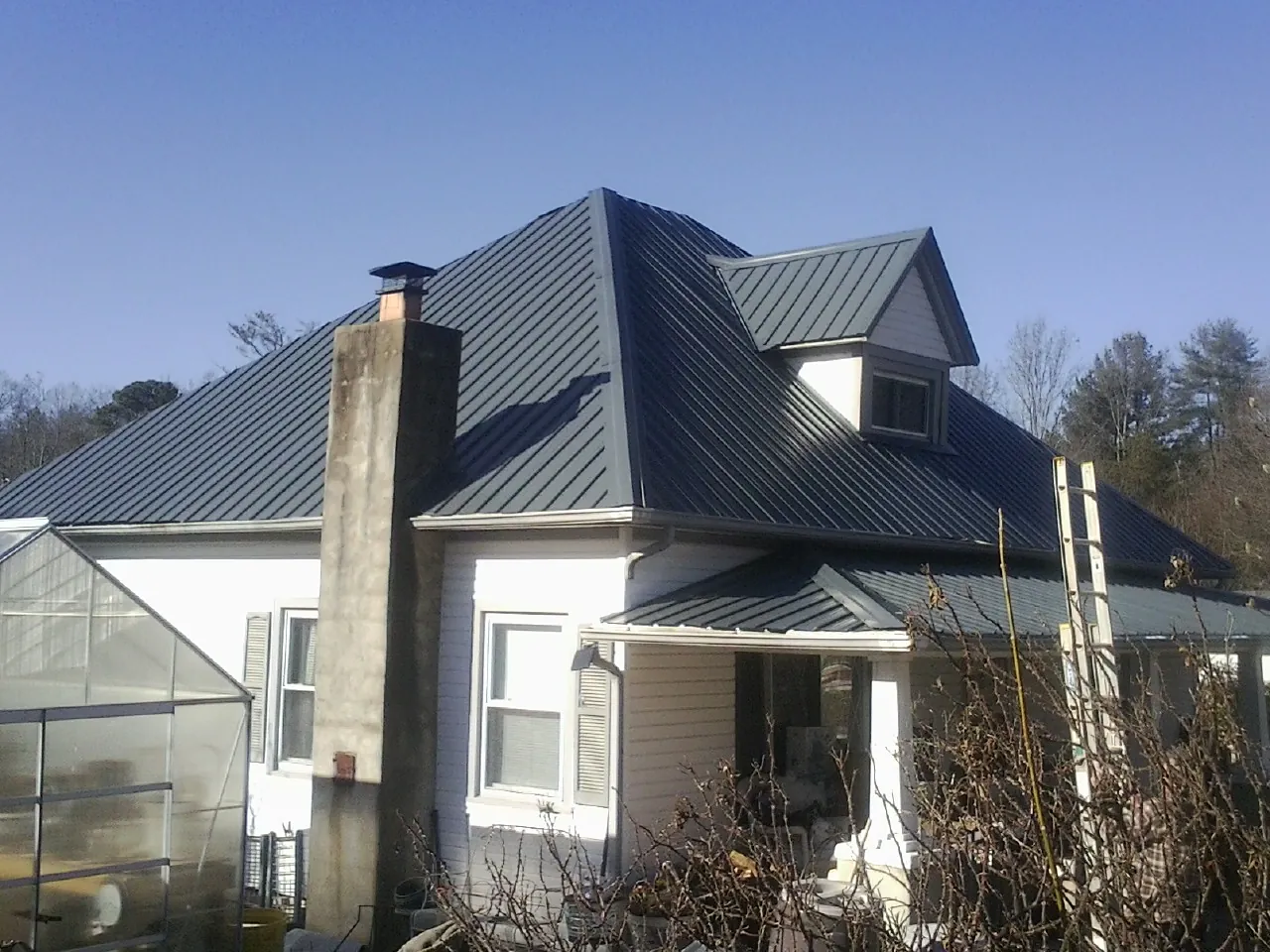 Dark blue standing seam metal roof on a white farmhouse with dormer — Slate & Tile Roof Repair by Roofing Brothers in Leonidas