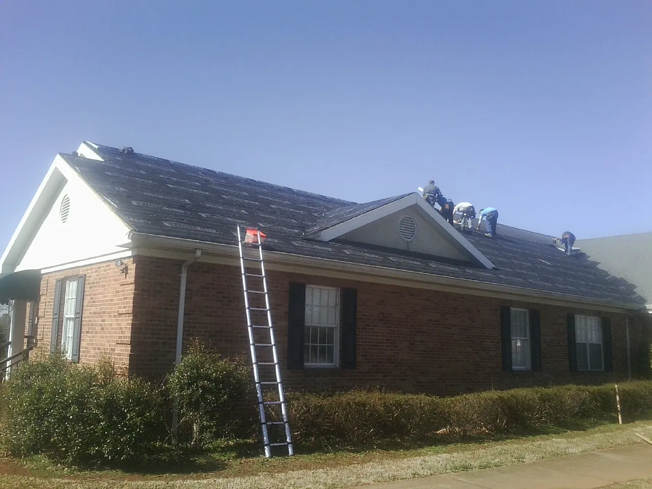 Crew tearing shingles off a brick ranch roof with a ladder set — Emergency Roof Repair work by our crew in Leonidas