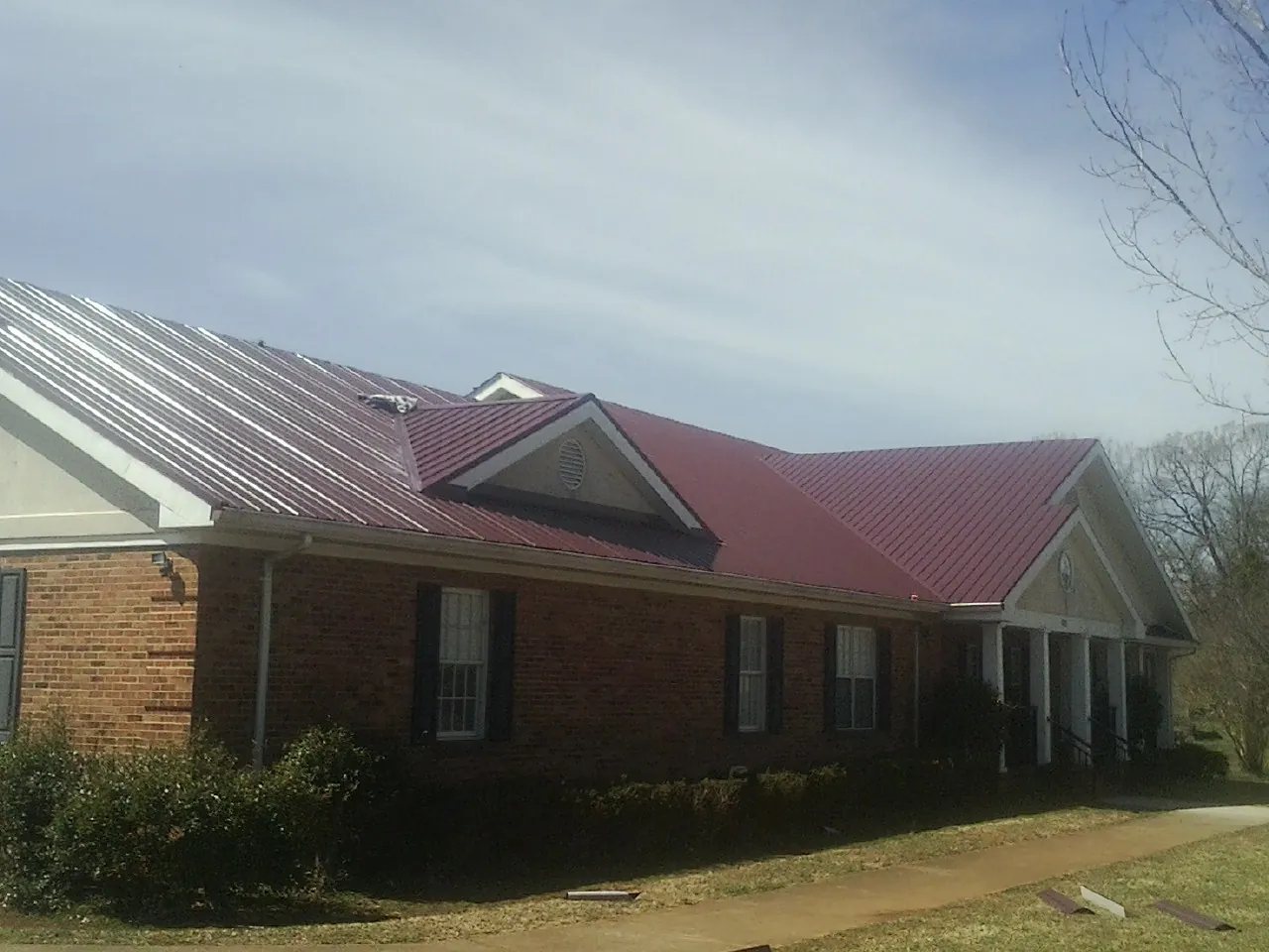 Red metal roof with gabled entries on a long brick building, from a Hail Damage Roof Repair job in Leonidas
