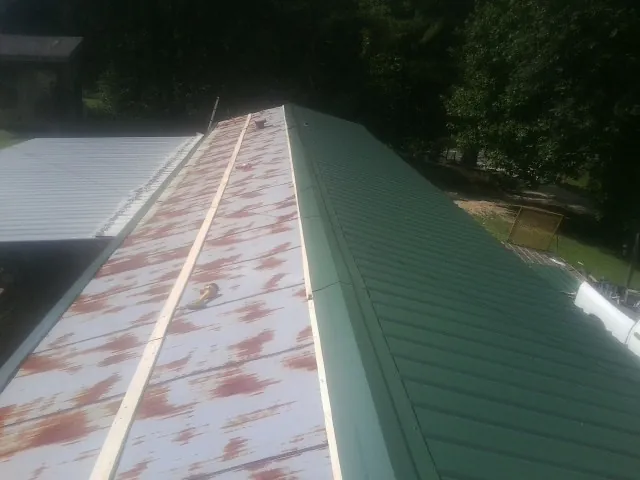 Old rusted panels beside newly installed green metal roofing — Wind Damage Roof Repair by Roofing Brothers in Leonidas