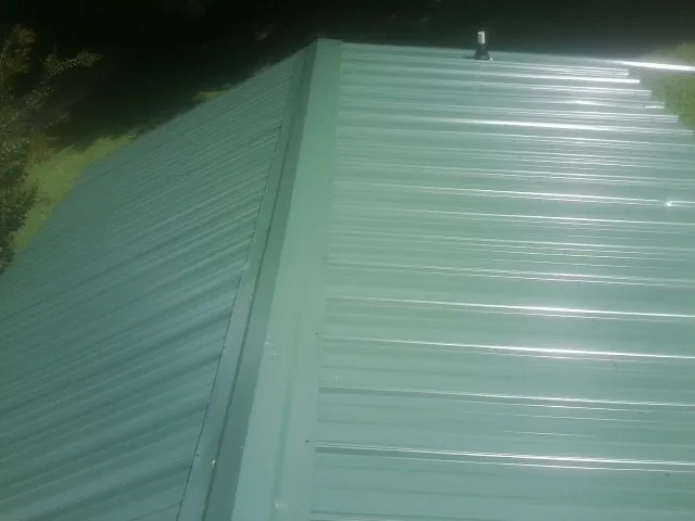 New green metal panels meeting at the ridge of a roof — Flat Roof Repair work by our crew in Leonidas