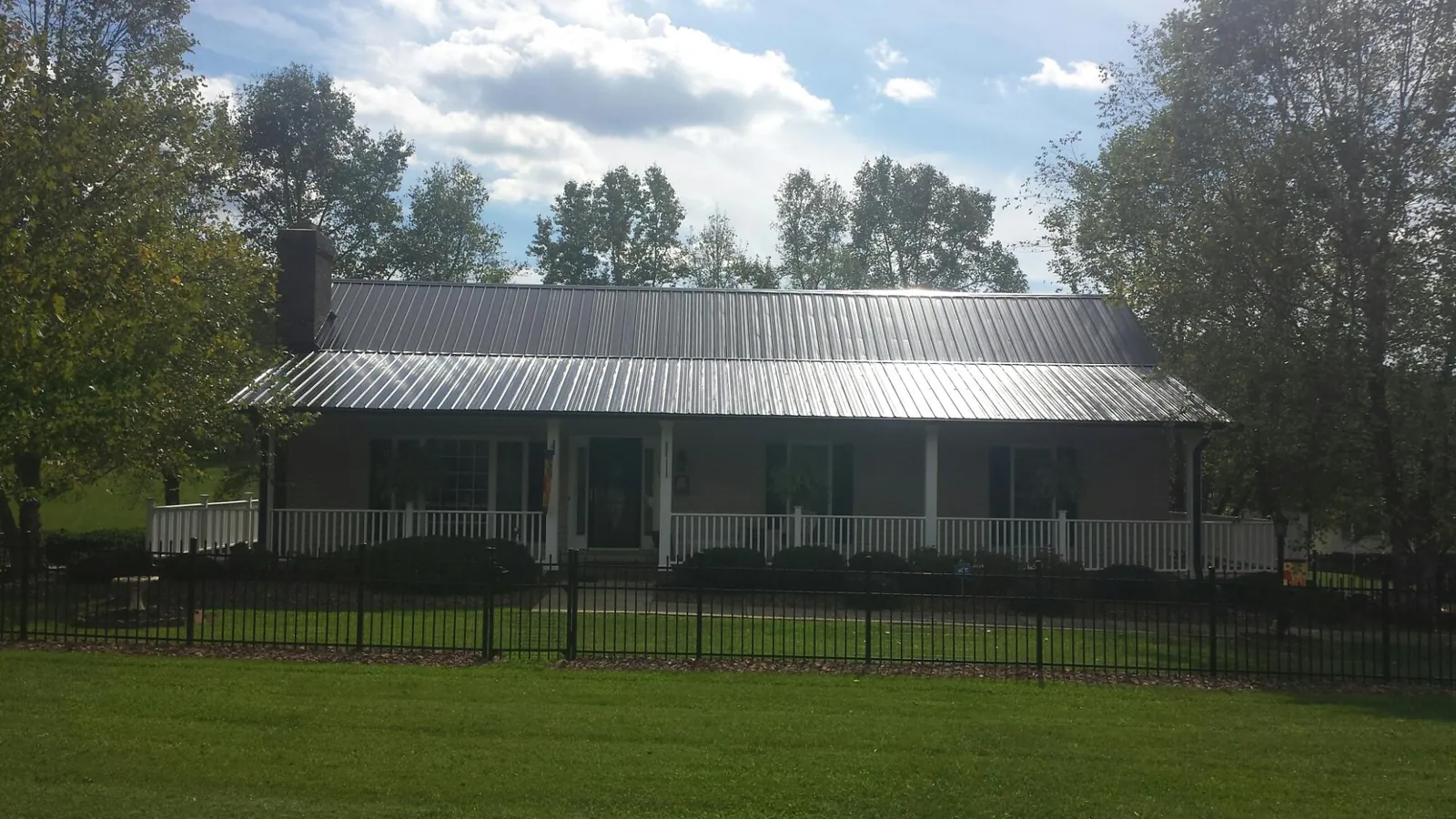 Gray metal roof on a brick ranch with a full width front porch — Gutter Guard Installation work by our crew in Leonidas