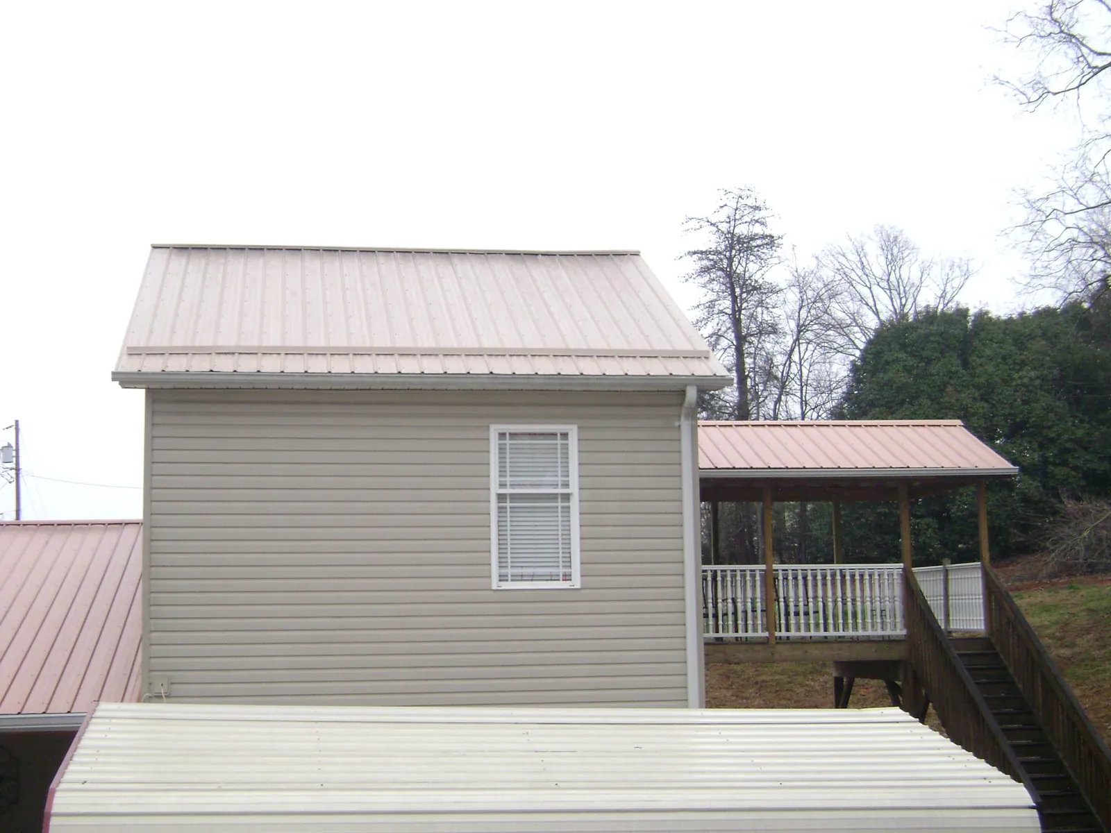 Tan metal roofs on a two story addition and attached porch, from a Roof Replacement job in Leonidas